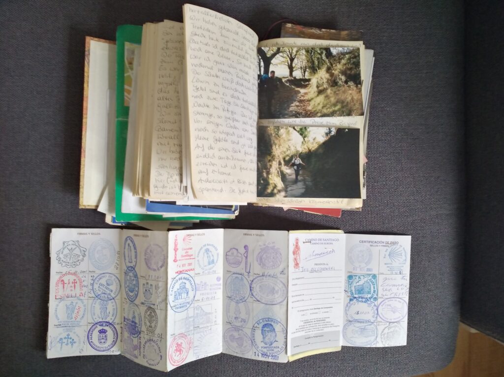 ein Pilgerausweis vom Jakobsweg und ein Pilgertagebuch mit handgeschriebenem Text und Fotos