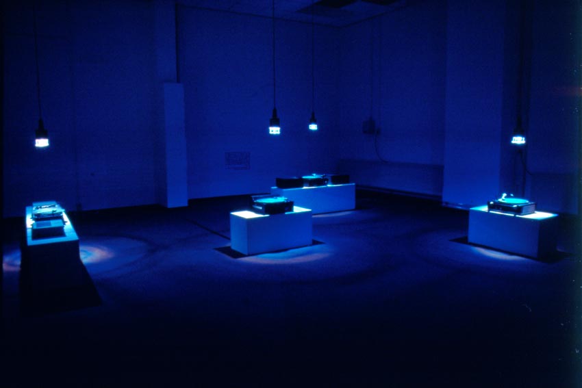 mehrere Plattenspieler stehen auf Podesten in einem blau beleuchteten Raum