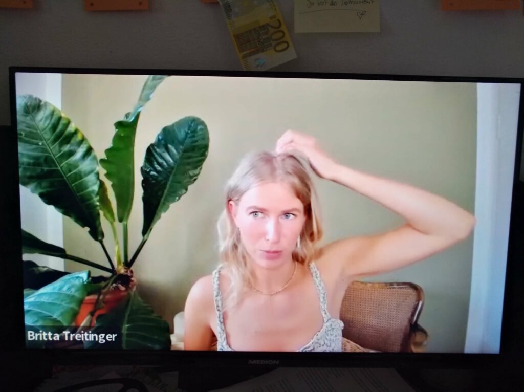 ein PC-Bildschirm, eine junge Frau mit blonden Haaren in enem Sommerkleid klopft sich mit den Fingern auf den Kopf