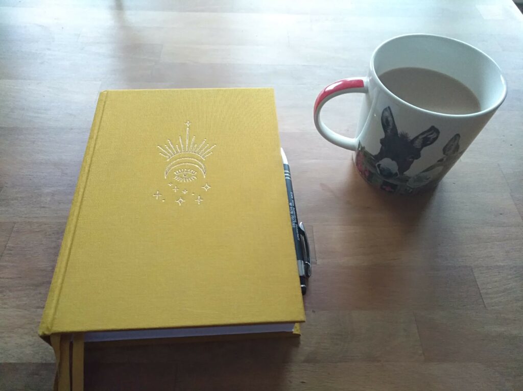 eine Tasse Kaffee auf einem Tisch, daneben ein gelbes Notizbuch