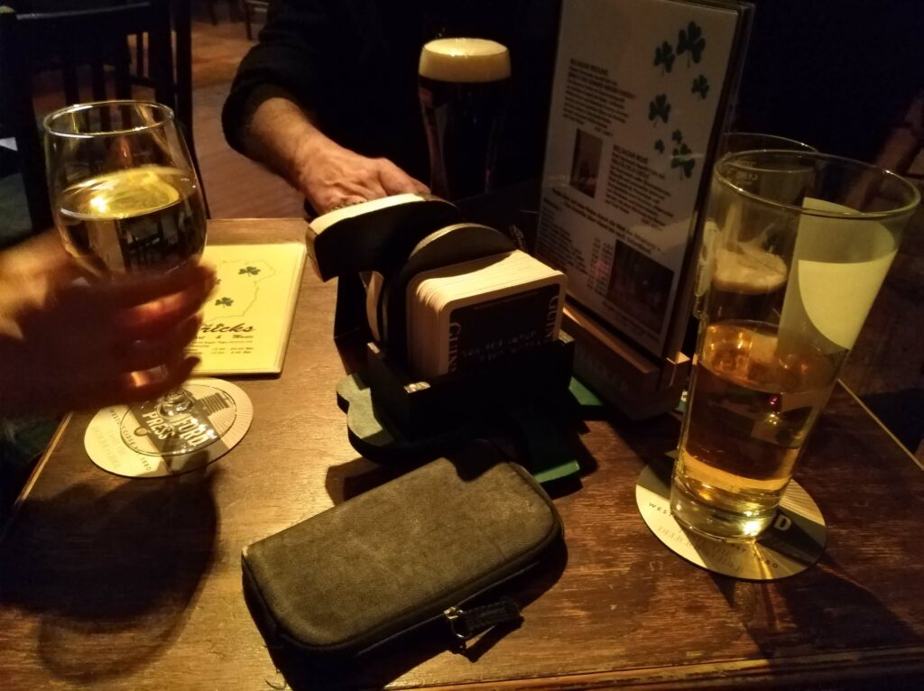 ein Tisch in einem Irish Pub, vier Gläser mit Wein, Bier und Cider, ein Mäppchen und Bierdeckel daneben