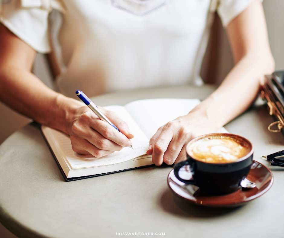 eine Frau sitzt mit einer Tasse Cappuccino an einem Tisch zum Journaling oder Tagebuchschreiben