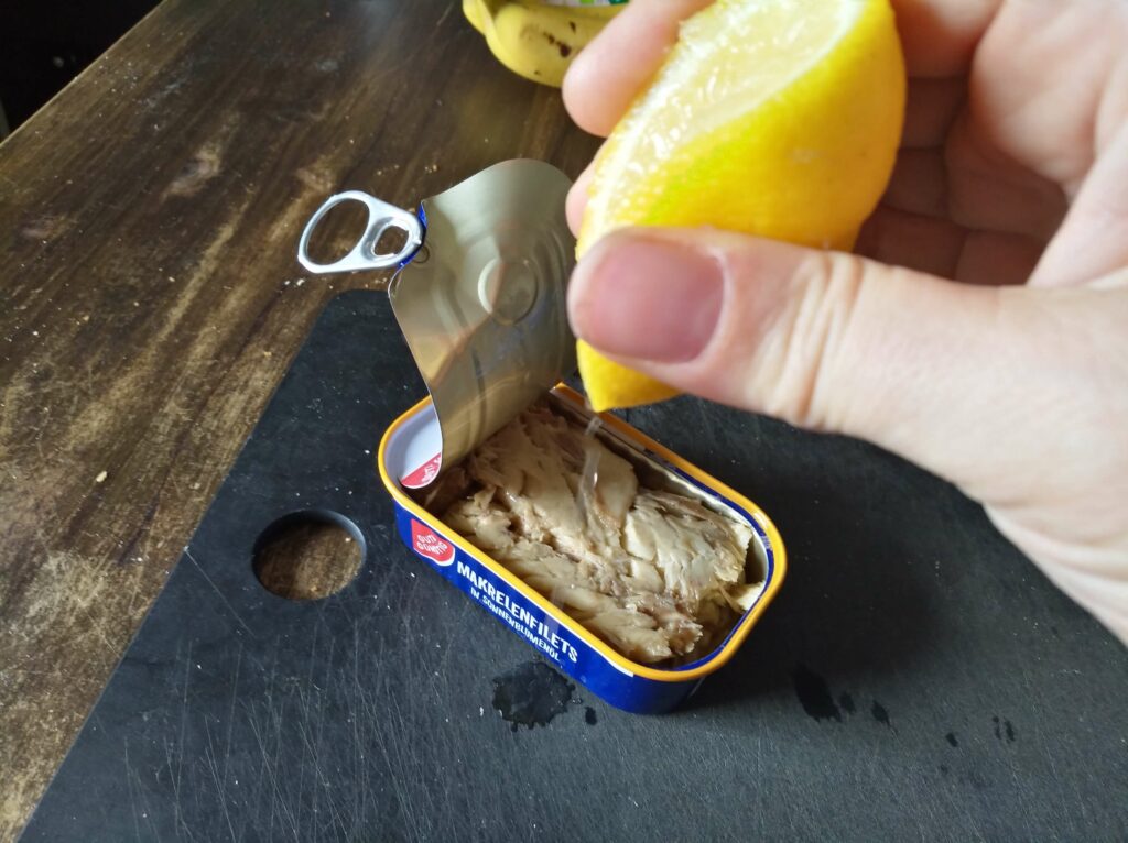 Zitrone wird auf eine Dose Makrelenfilets geträufelt