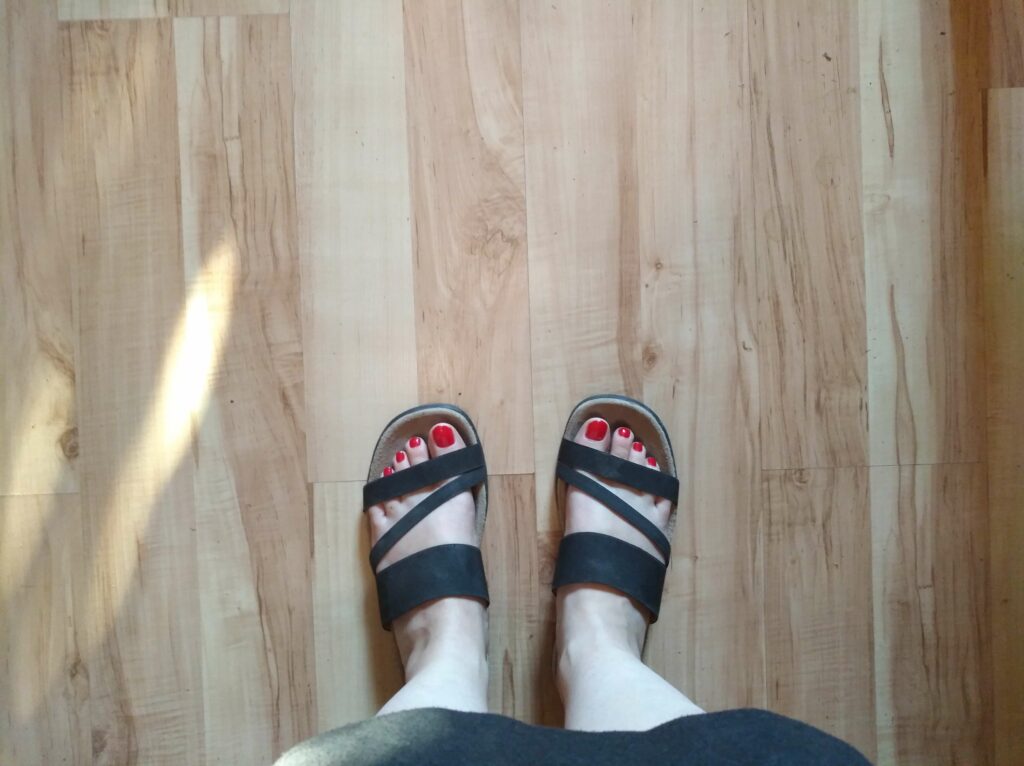 Frauenfüße in schwarzen Sandalen mit rot lackierten Fußnägeln