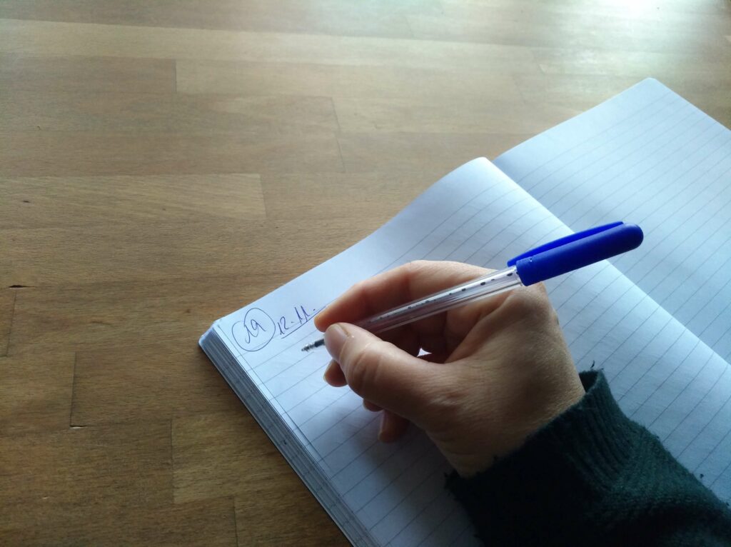 ein aufgechlagenes Notizbuch zum 12.11. und eine Hand, die einen Stift hält und bereit ist zum Schreiben